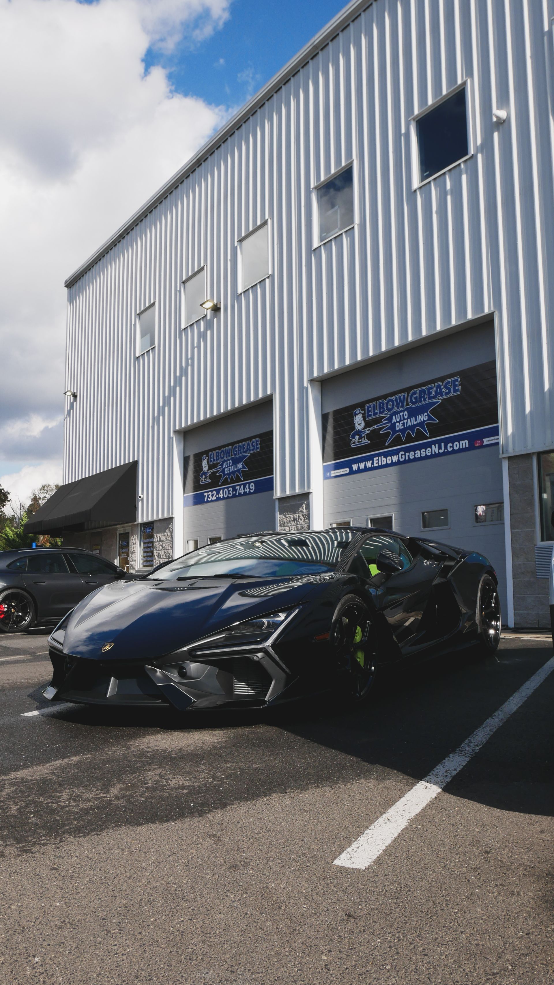 Black sports car parked outside a modern metal-sided building on a sunny day