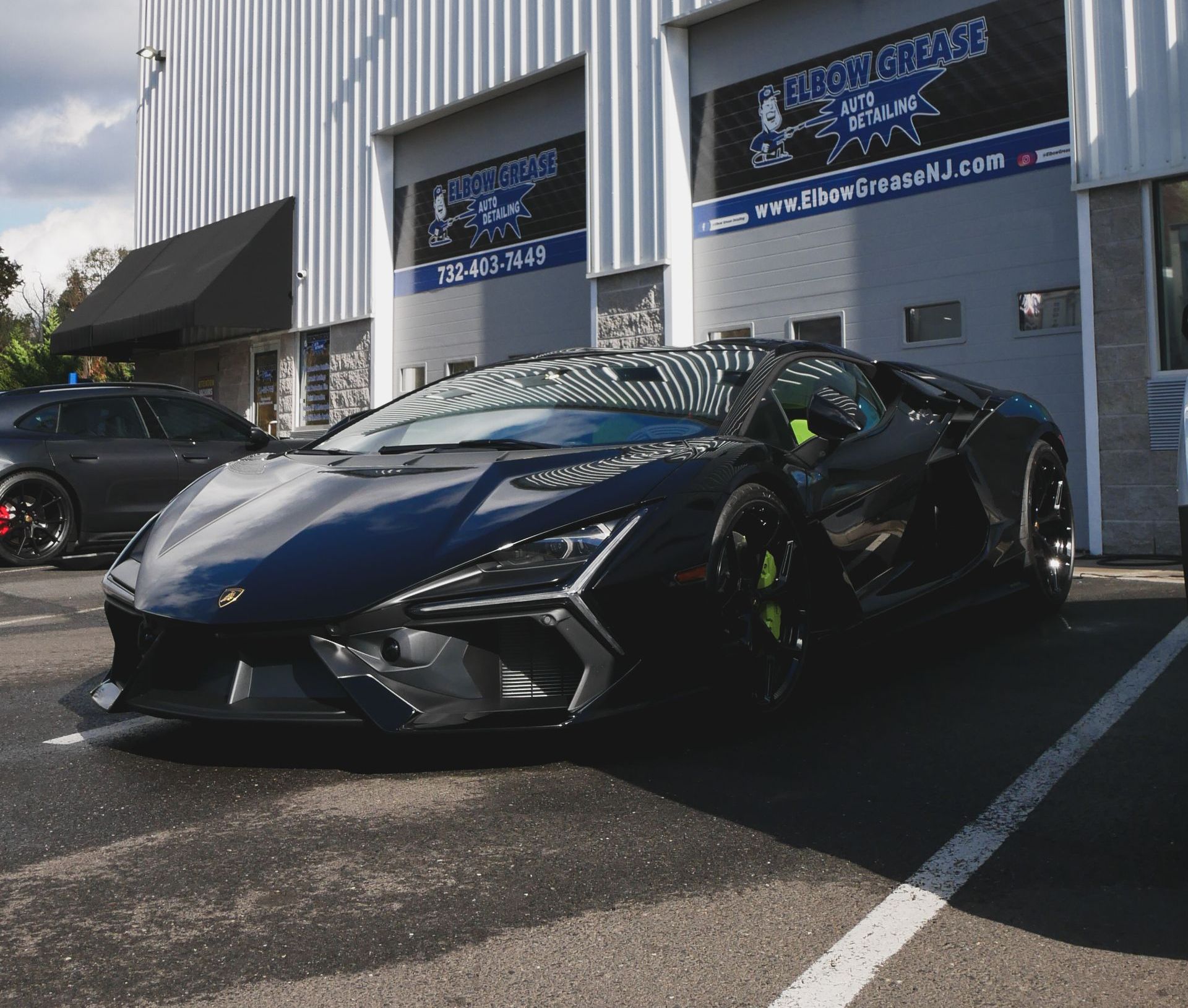 Black Lamborghini parked outside a shop in sunlight