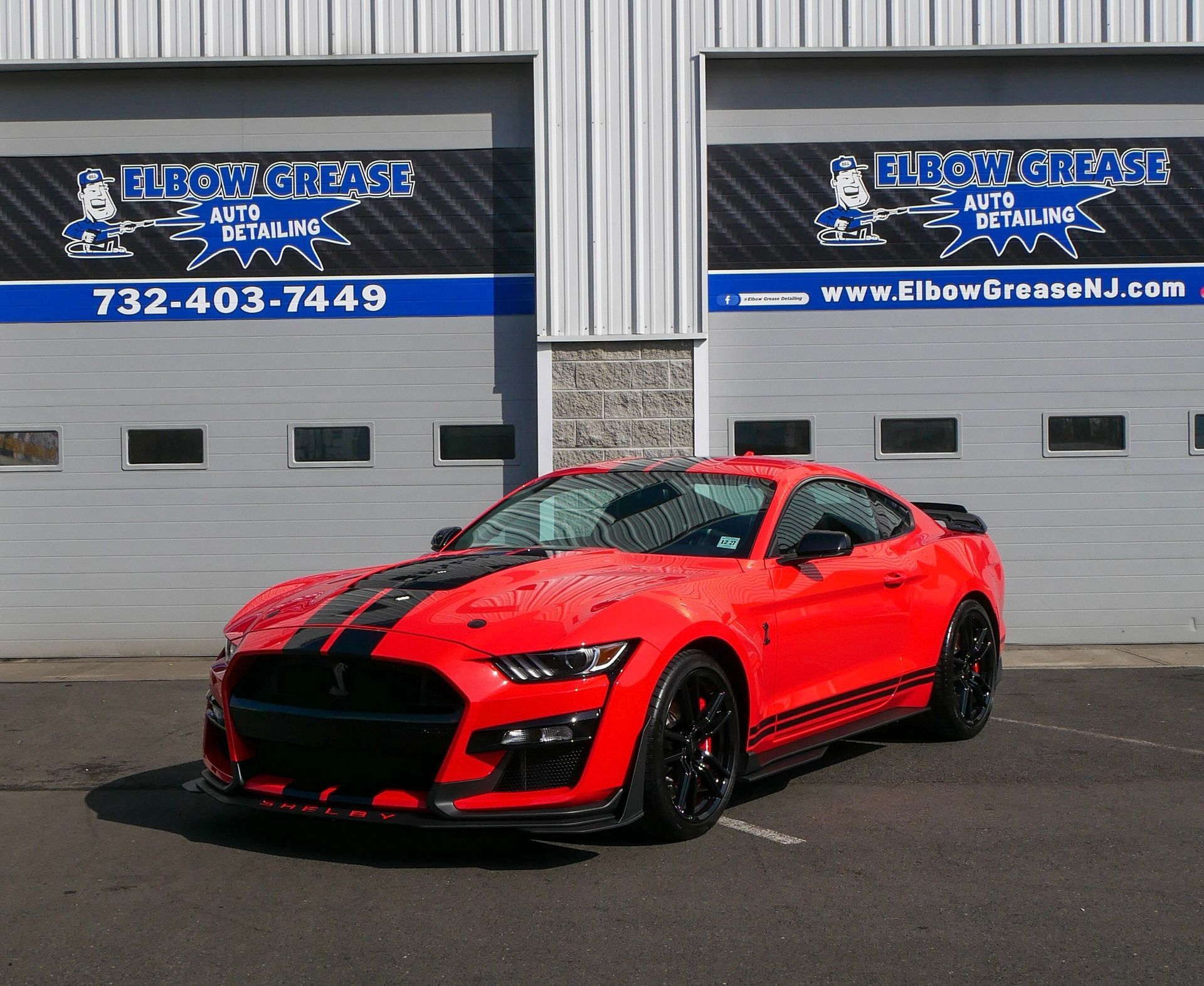 Red Ford Mustang Shelby in front of a garage with Elbow Grease Auto Detail sign.
