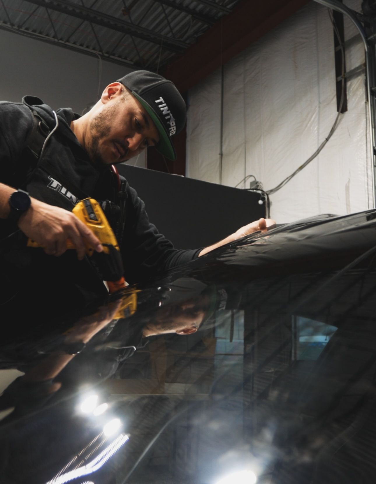 Worker using a yellow power tool on a car windshield in a garage