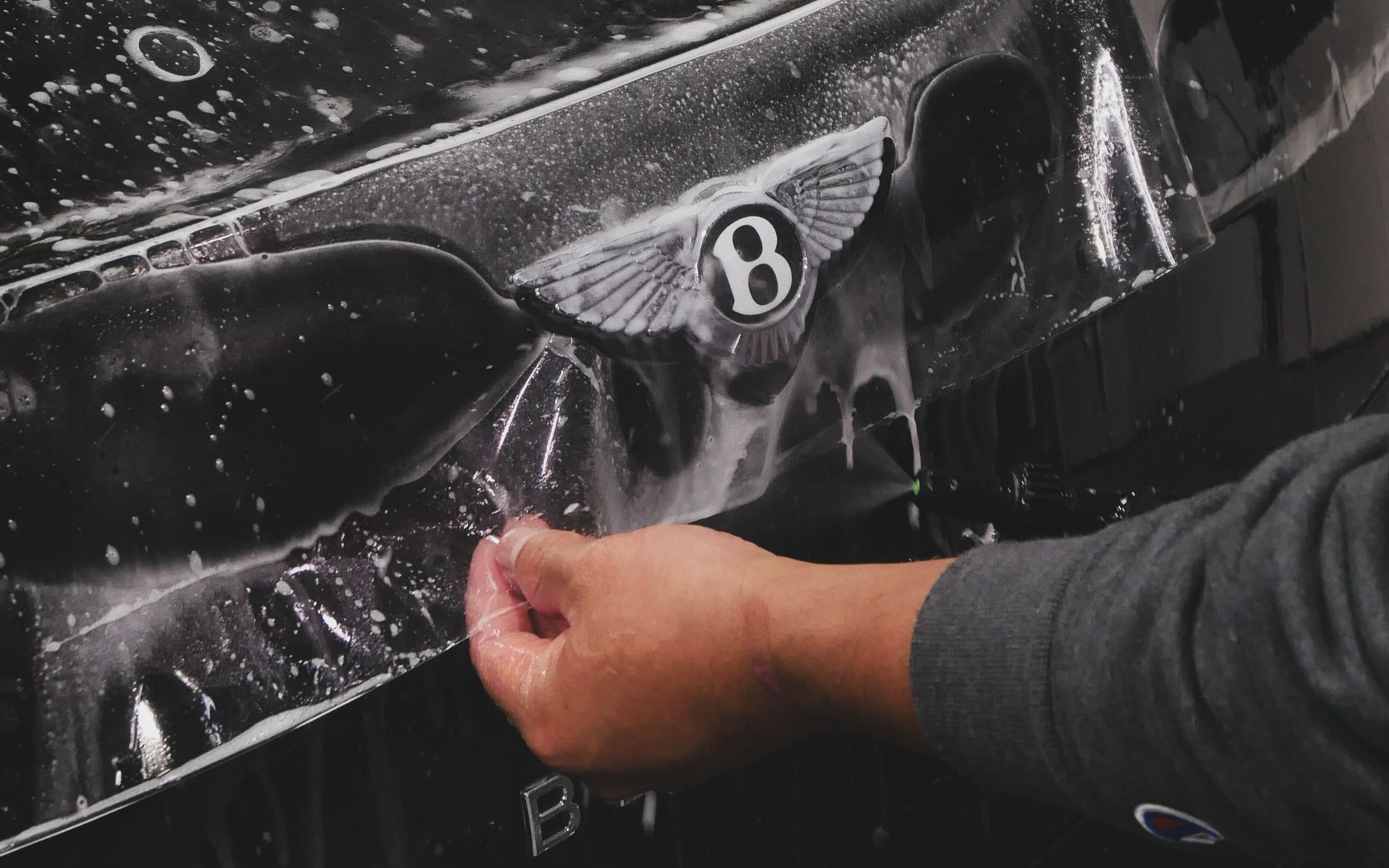 A person peeling protective film from a black Bentley emblem on a car.