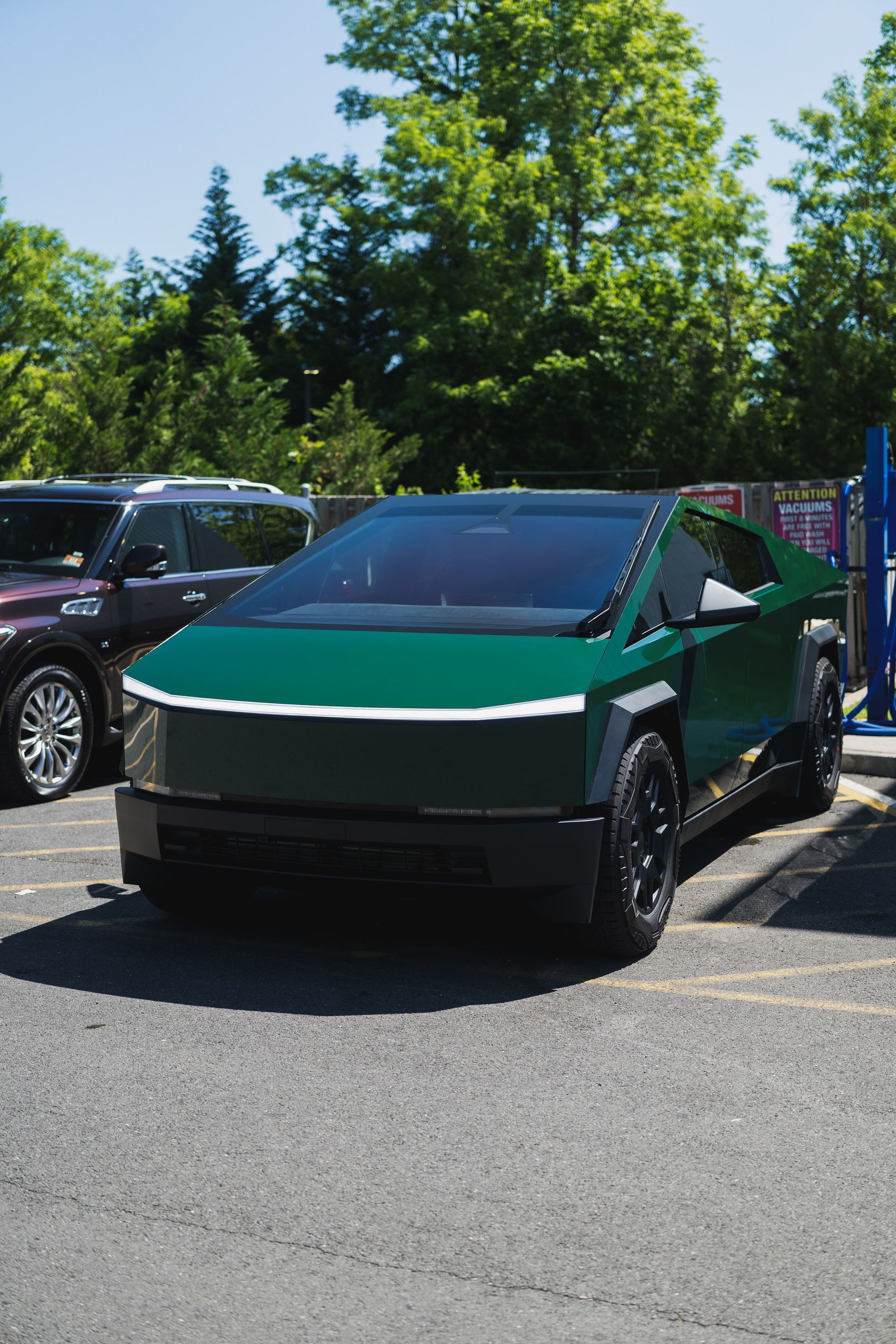 Green Cybertruck parked in a lot, front view with trees and other cars in the background