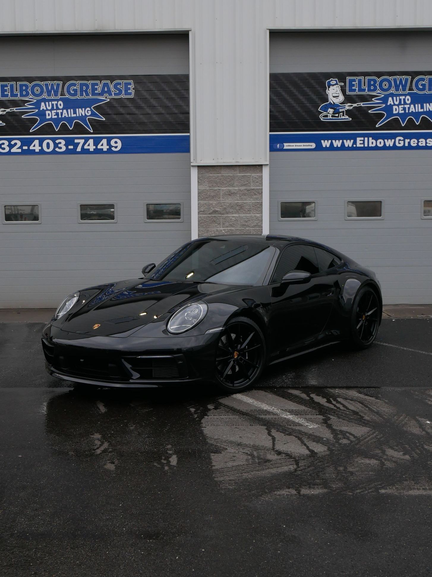 Black sports car parked outside a garage on a wet pavement.