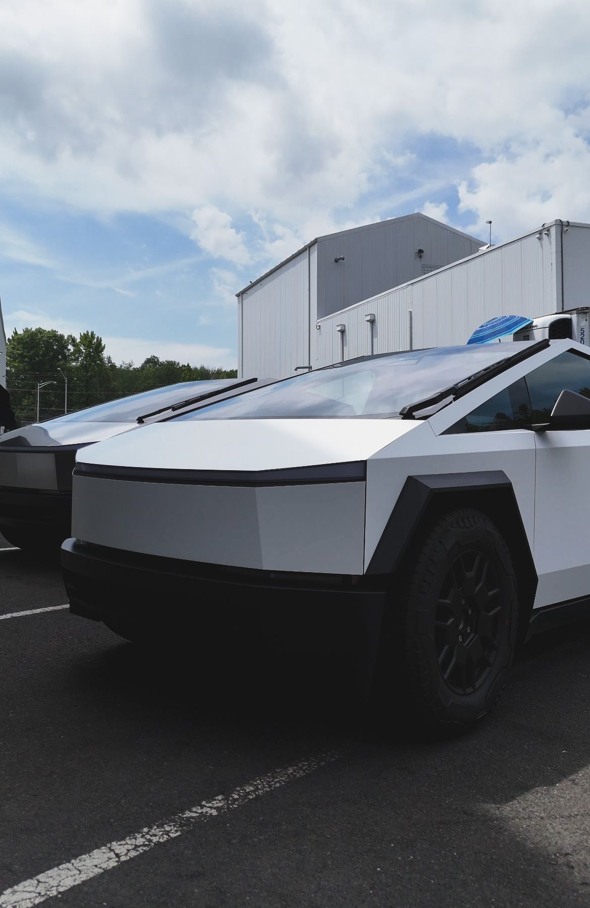 White Tesla Cybertruck parked outdoors on asphalt near a building under a cloudy sky