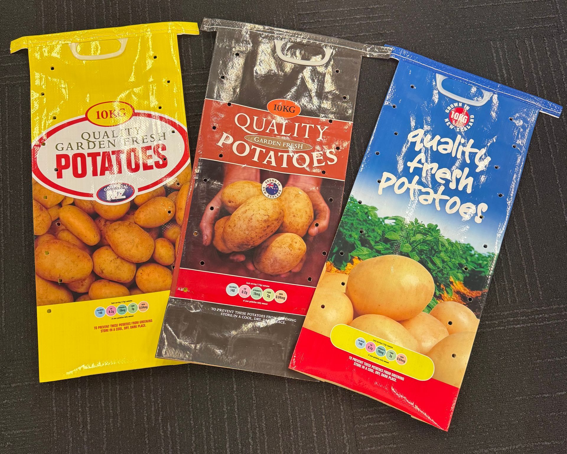 Three bags of potatoes in yellow, brown, and blue packaging on a dark surface.