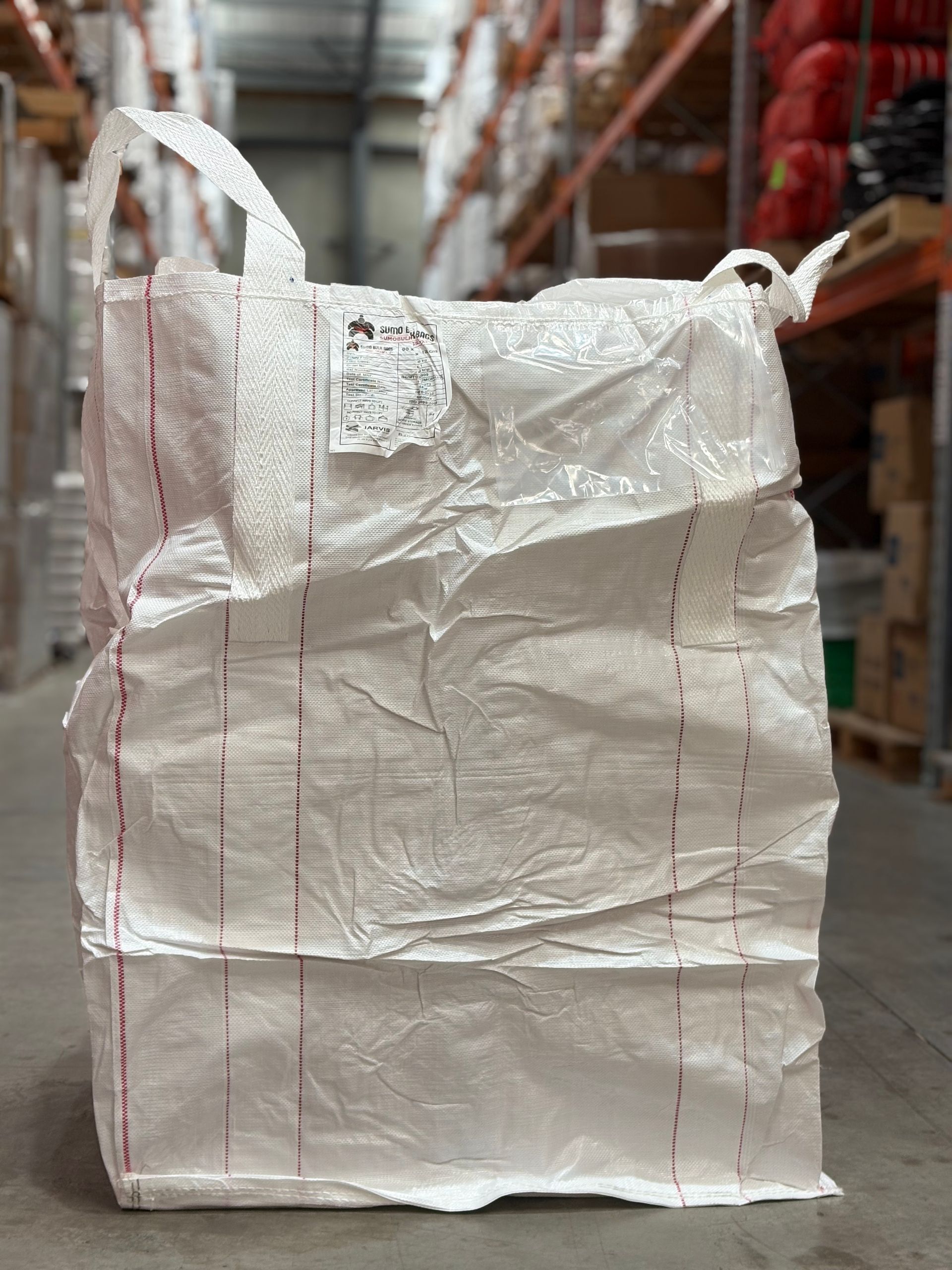 White insulated shipping bag standing in a warehouse aisle with shelves in the background
