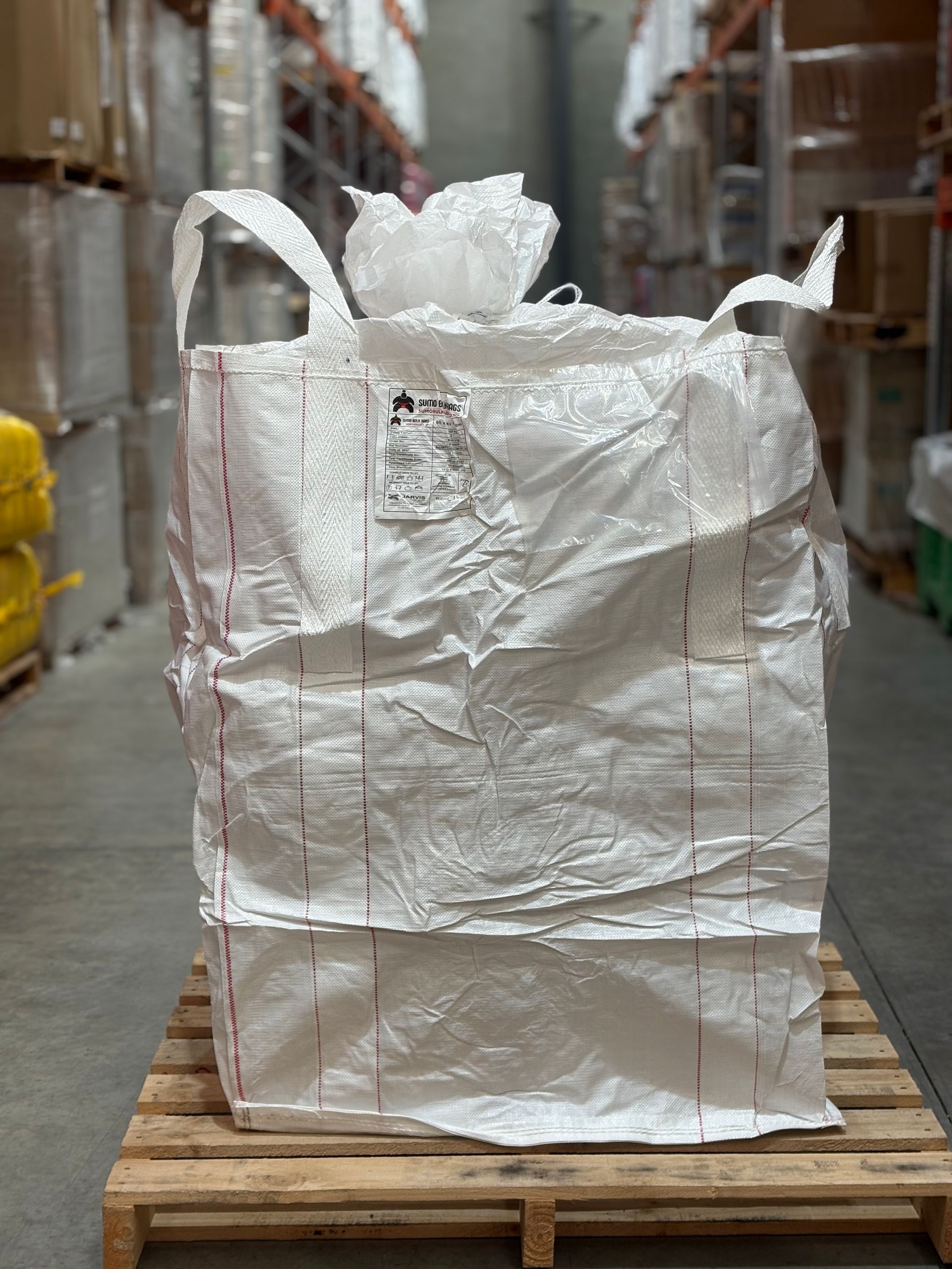 Large white bulk bag on a wooden pallet in a warehouse aisle