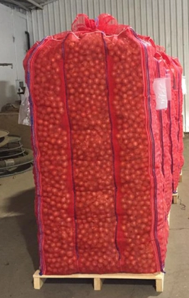 Red mesh bag of oranges on a wooden pallet in a warehouse.