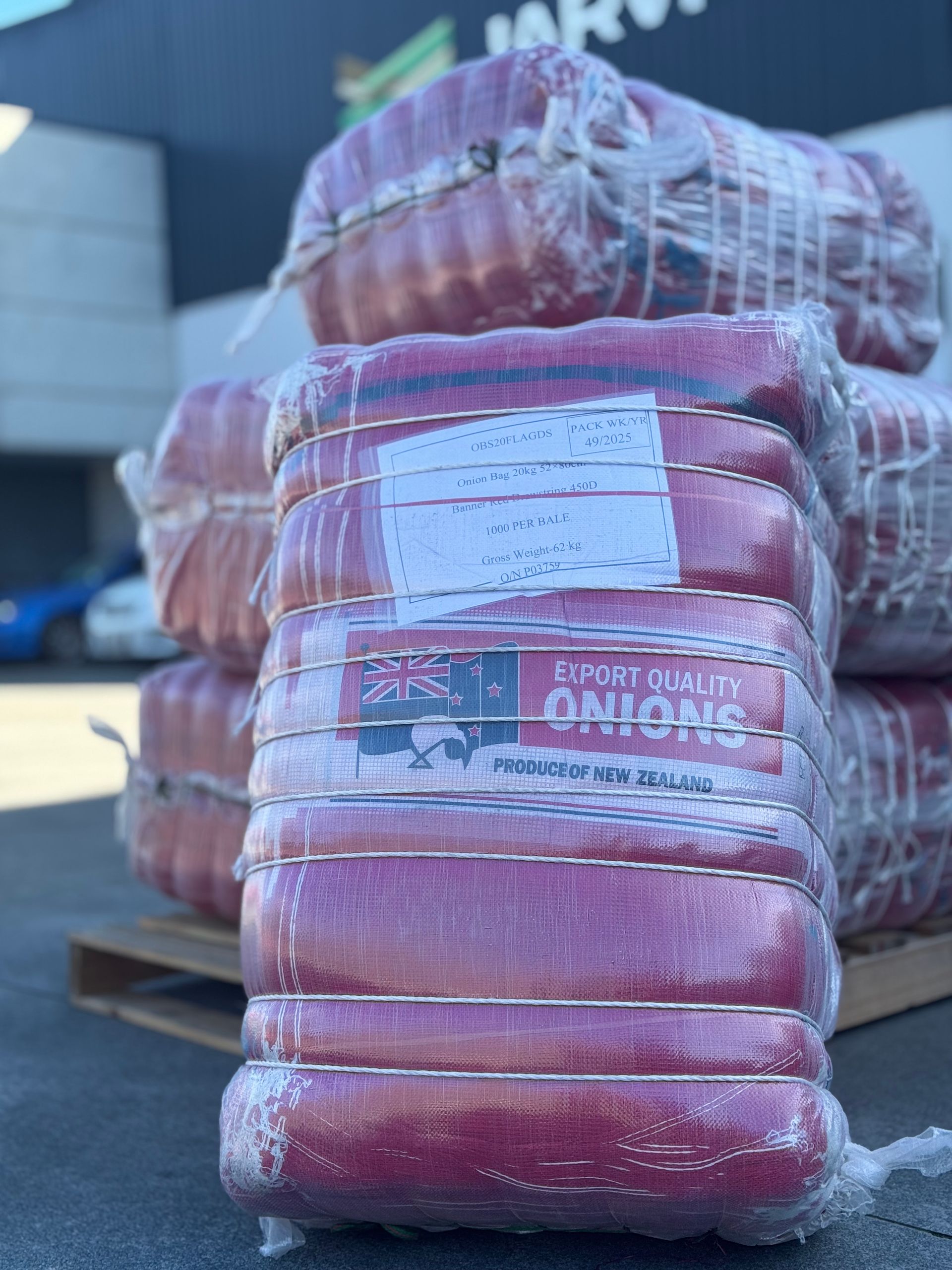Stacks of pink-red wrapped produce pallets outdoors, with a label on the front bundle.