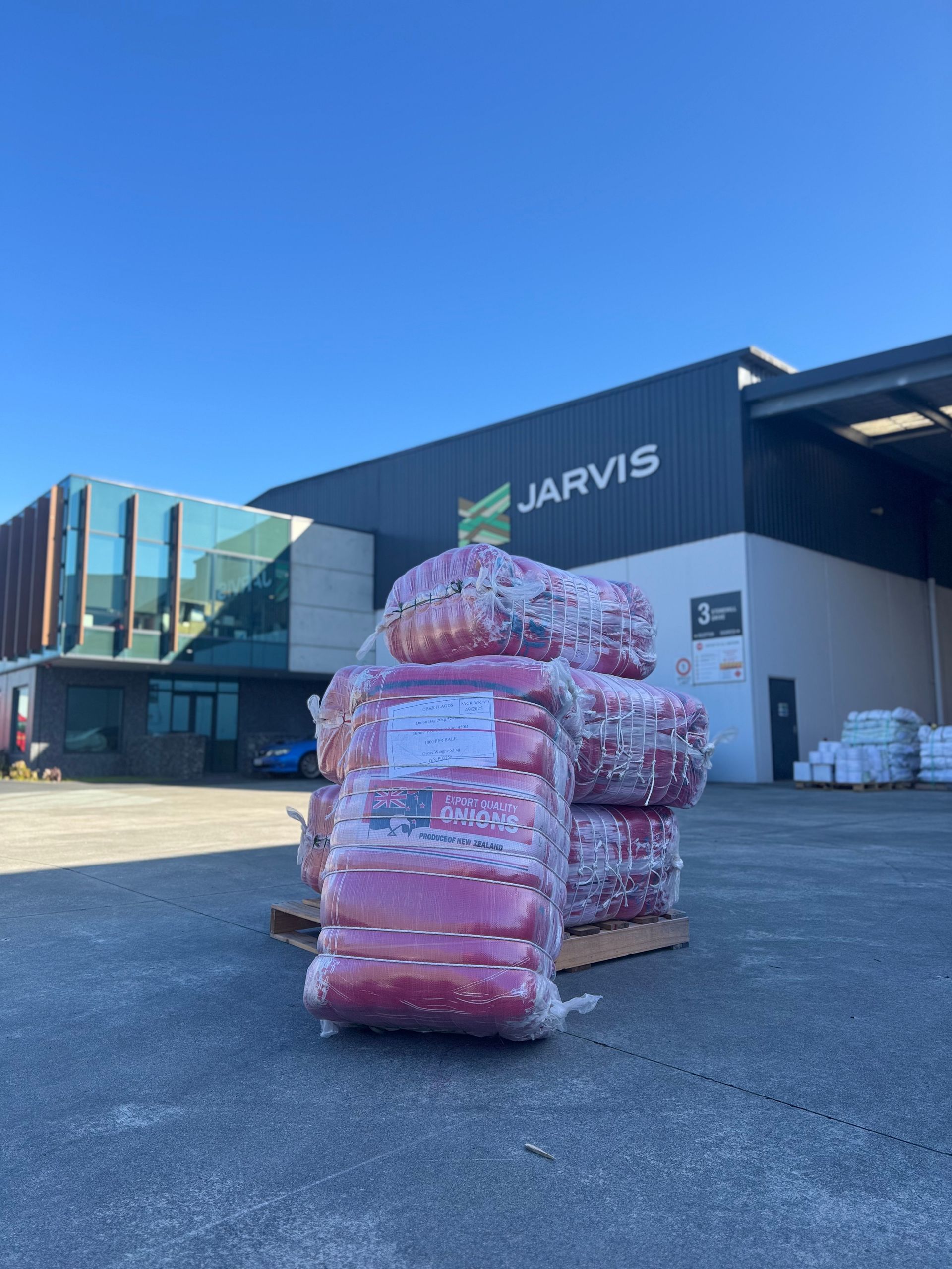 Stacks of pink-wrapped packages on a pallet outside a Jarvis warehouse under a blue sky