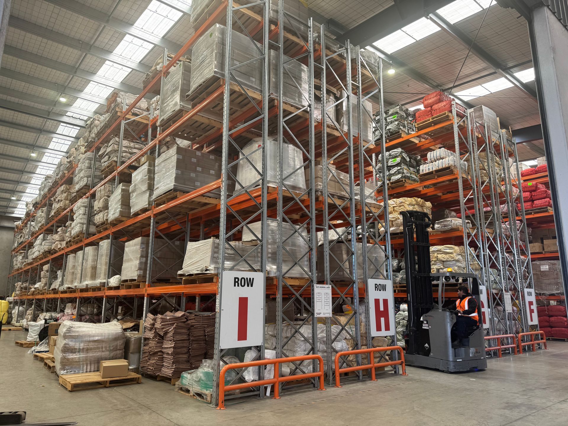 Warehouse racks stacked with pallets and goods, forklift operating in an aisle