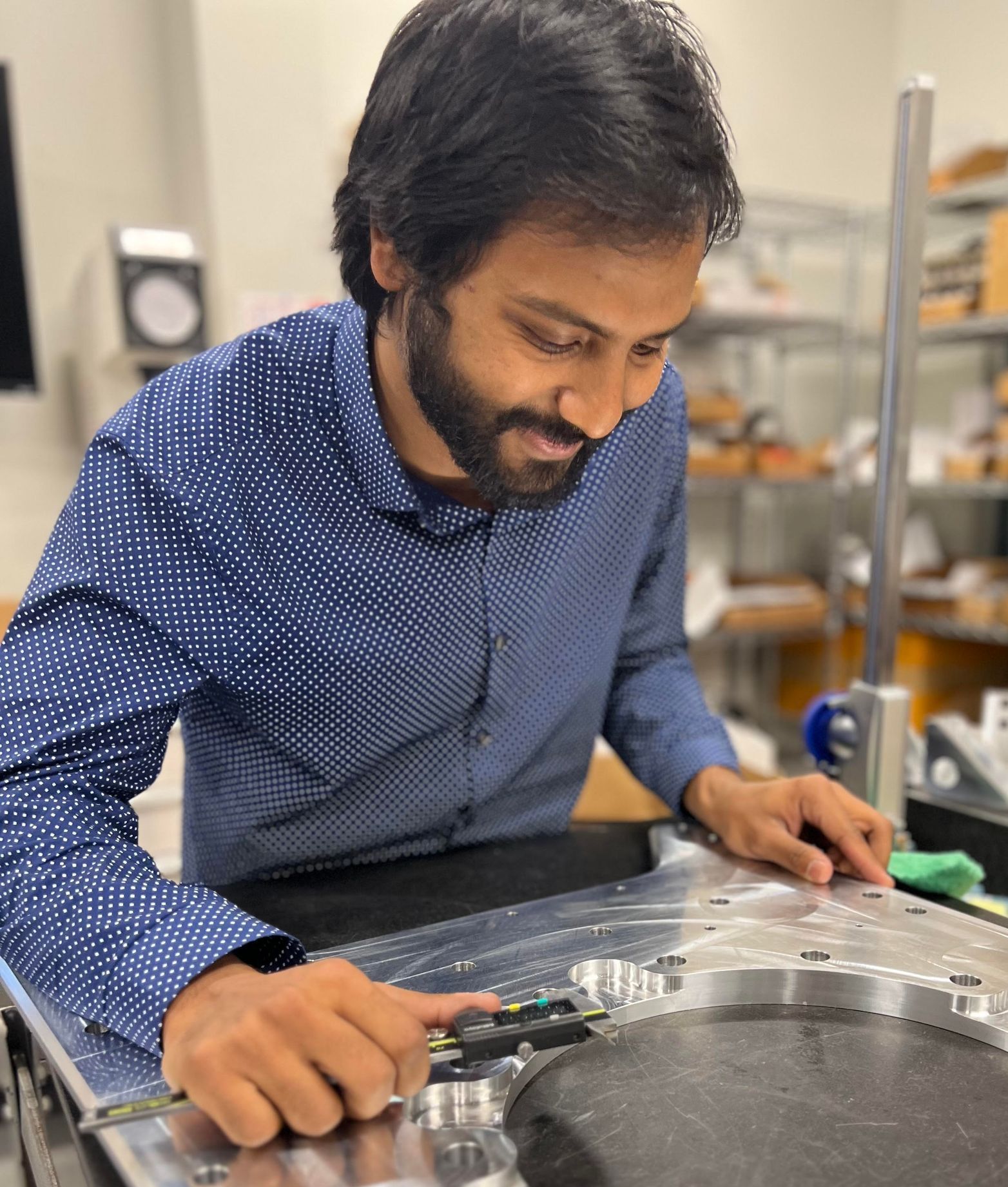 A man in a blue shirt is measuring a piece of metal.