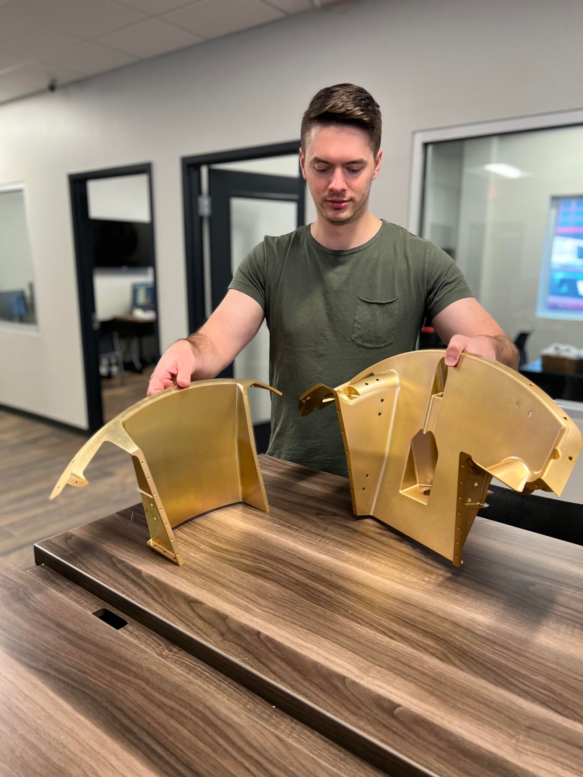 A man is standing next to two pieces of metal on a wooden table.