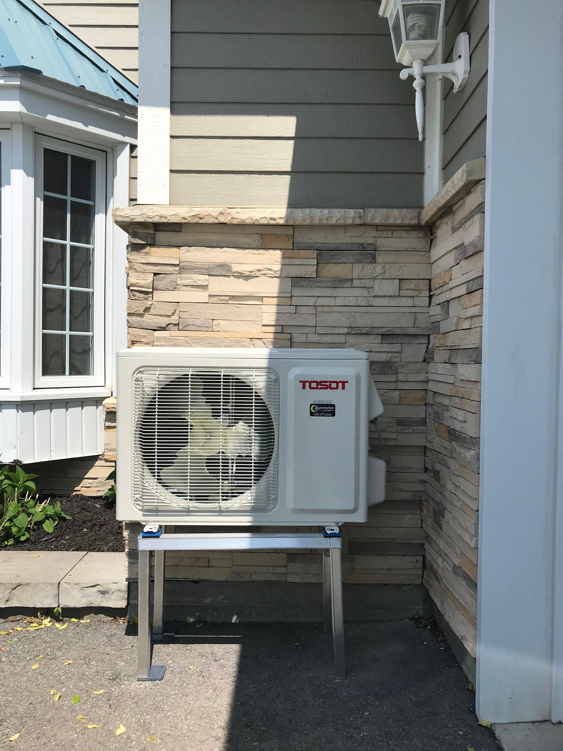 Unité de climatisation sur un support à côté d'un bâtiment en pierre et à bardage.