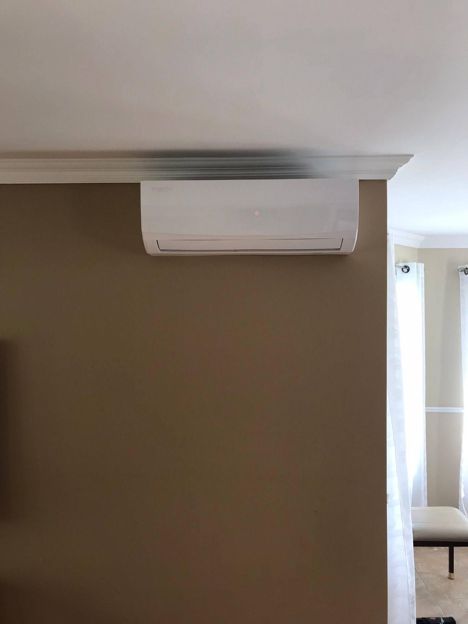 Climatiseur split blanc fixé sur un mur marron, sous une moulure blanche.