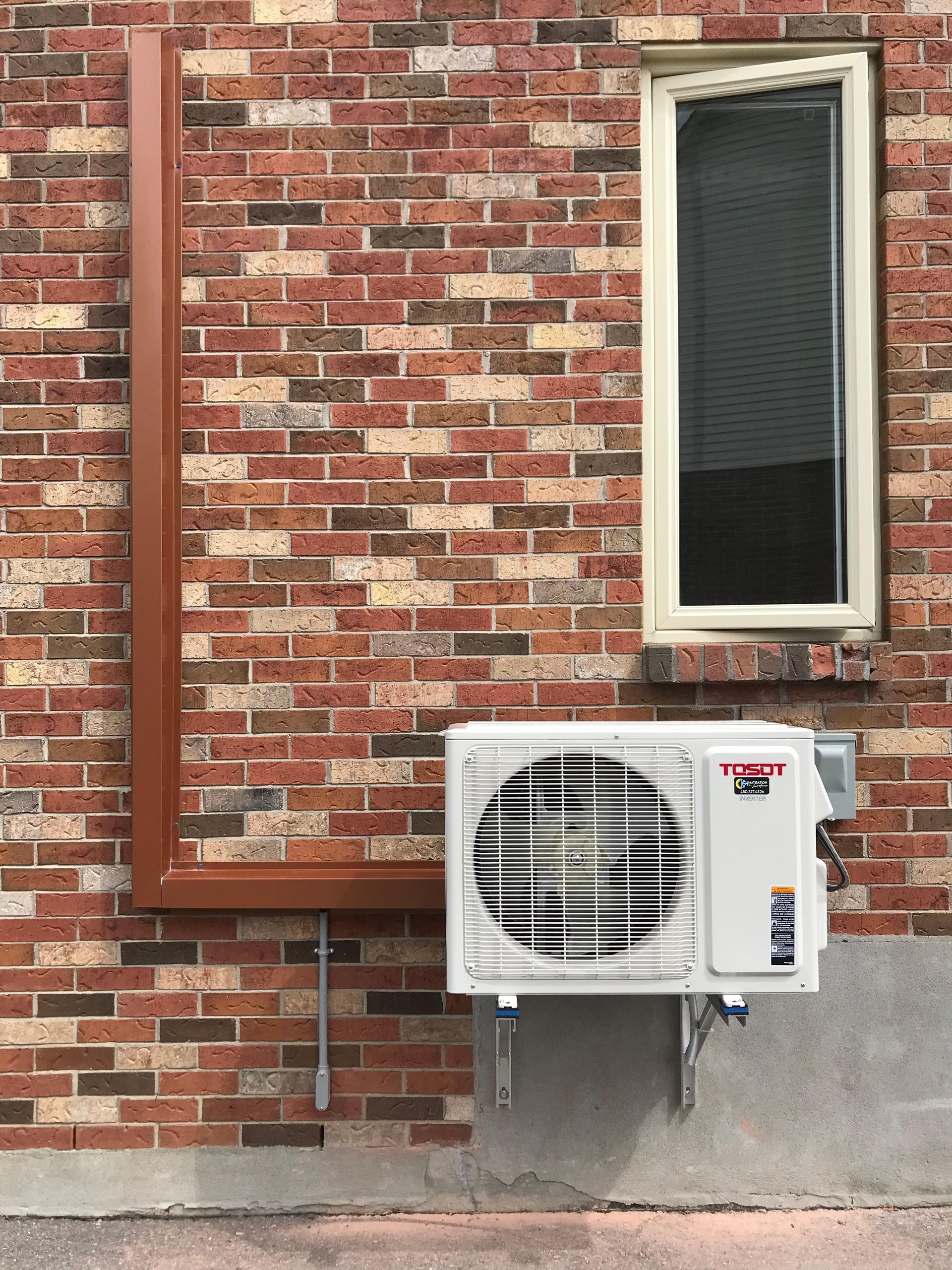 Vue extérieure d'un mur en briques avec un climatiseur split installé et une fenêtre.