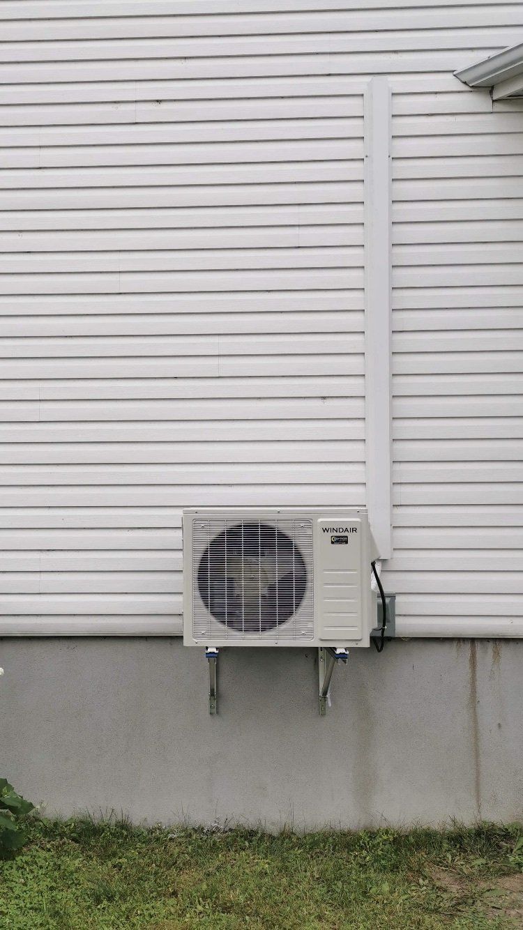 Unité de climatisation extérieure montée sur le revêtement blanc d'un bâtiment, avec un conduit de protection ascendant.