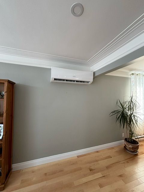 Climatiseur fixé sur un mur gris dans une pièce avec parquet.