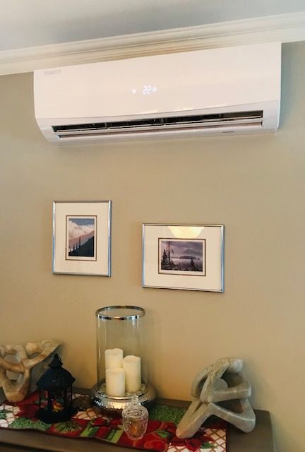 Climatiseur mural blanc au-dessus d'une table décorative avec deux tableaux encadrés sur un mur beige.