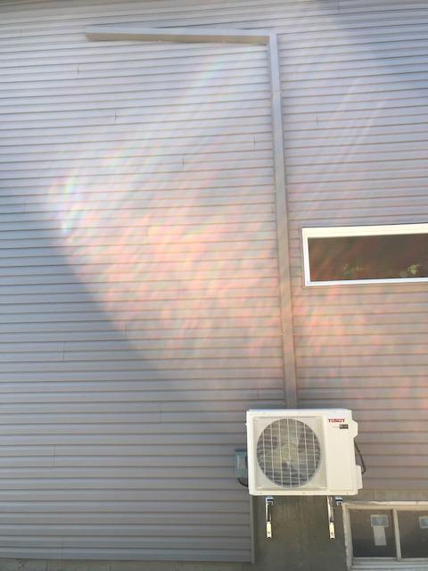 Mur extérieur avec unité de climatisation. La lumière du soleil se reflète sur le revêtement et une fenêtre est visible.