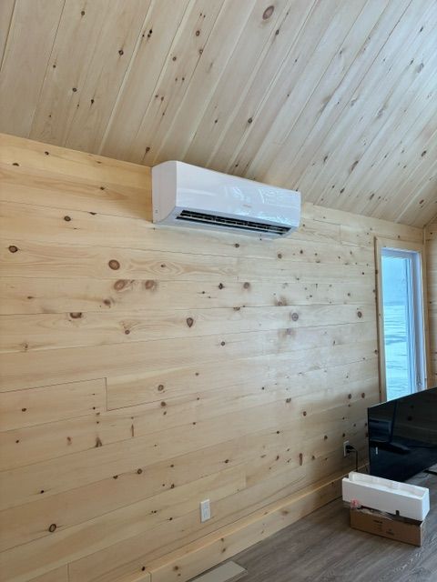 Climatiseur blanc fixé sur un mur lambrissé, près d'une fenêtre, à l'intérieur d'une pièce.