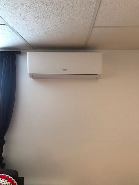 Climatiseur blanc sans conduit, fixé sur un mur blanc sous un plafond.