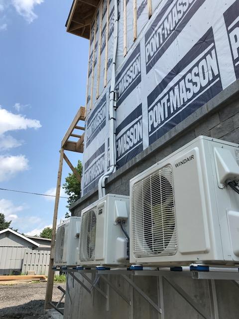 Unités de climatisation extérieures installées sur le côté d'un bâtiment en construction, ciel bleu en arrière-plan.