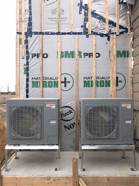 Deux unités de climatisation grises, montées sur des supports métalliques, sont adossées à la façade d'un bâtiment.