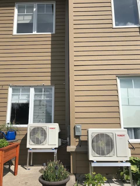 Deux unités de climatisation beiges sur des supports argentés, installées à l'extérieur d'un bâtiment beige avec des fenêtres.