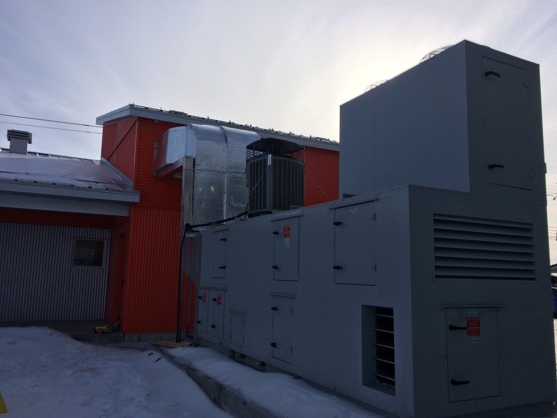 Gros équipements industriels gris à côté d'un bâtiment au bardage orange ; neige au sol.