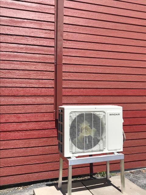 Unité de climatisation blanche sur un support métallique contre un mur en bois rouge.