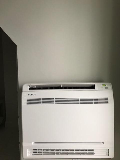 Unité de climatisation TIGGOT blanche fixée sur un mur gris.