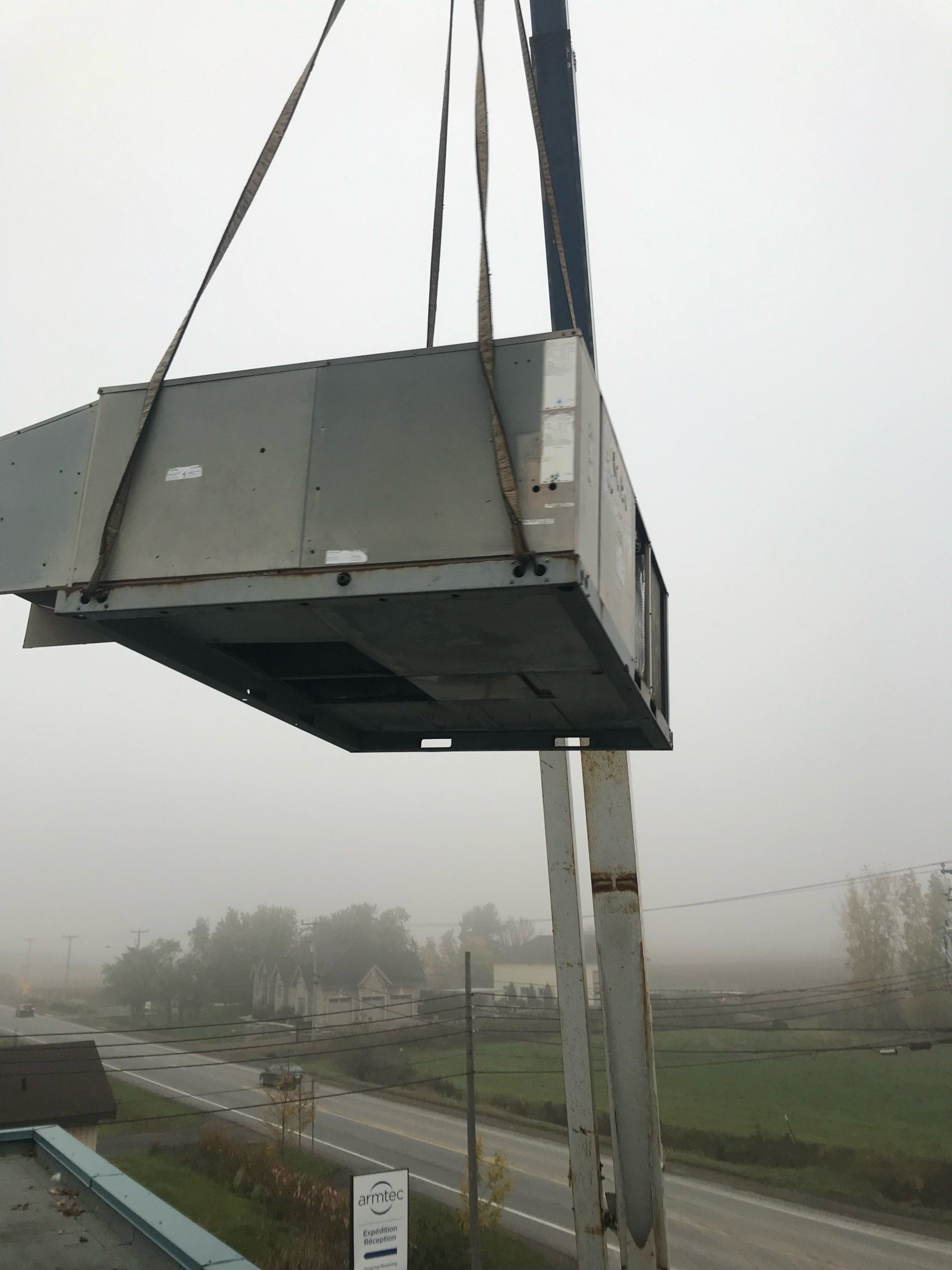 Unité de climatisation de grande taille suspendue par une grue, probablement destinée à être installée sur le toit d'un bâtiment.