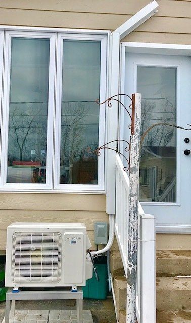 Extérieur d'un bâtiment beige avec une porte et une fenêtre blanches. Un climatiseur est installé en dessous.