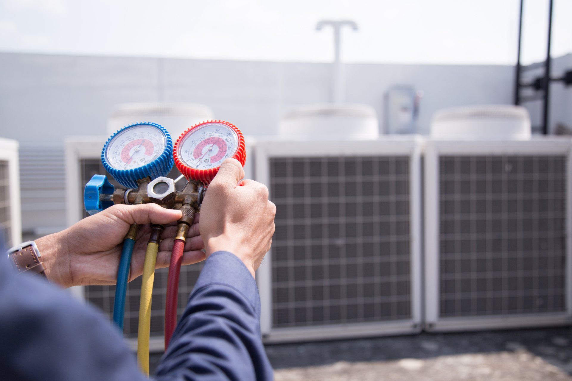 Une personne tenant un manomètre installé près d'unités de climatisation sur un toit.