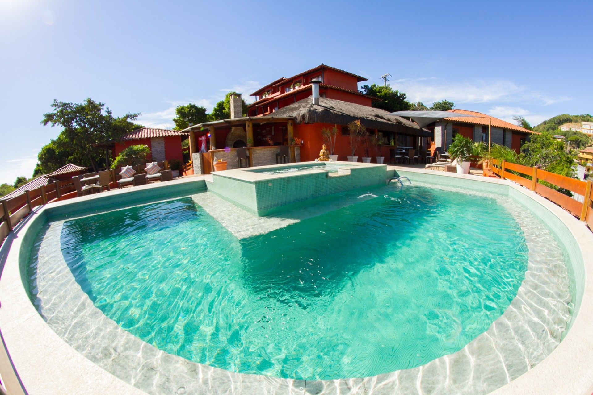 Piscina curva em tom turquesa diante de uma villa tropical com terraço e palmeiras