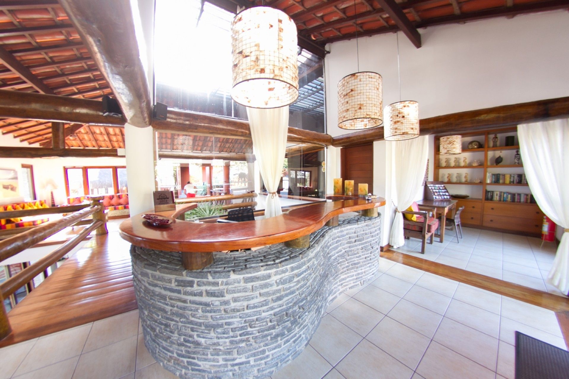 Interior de café rústico com balcão de pedra, luminárias suspensas e prateleiras ao longo da parede do fundo.