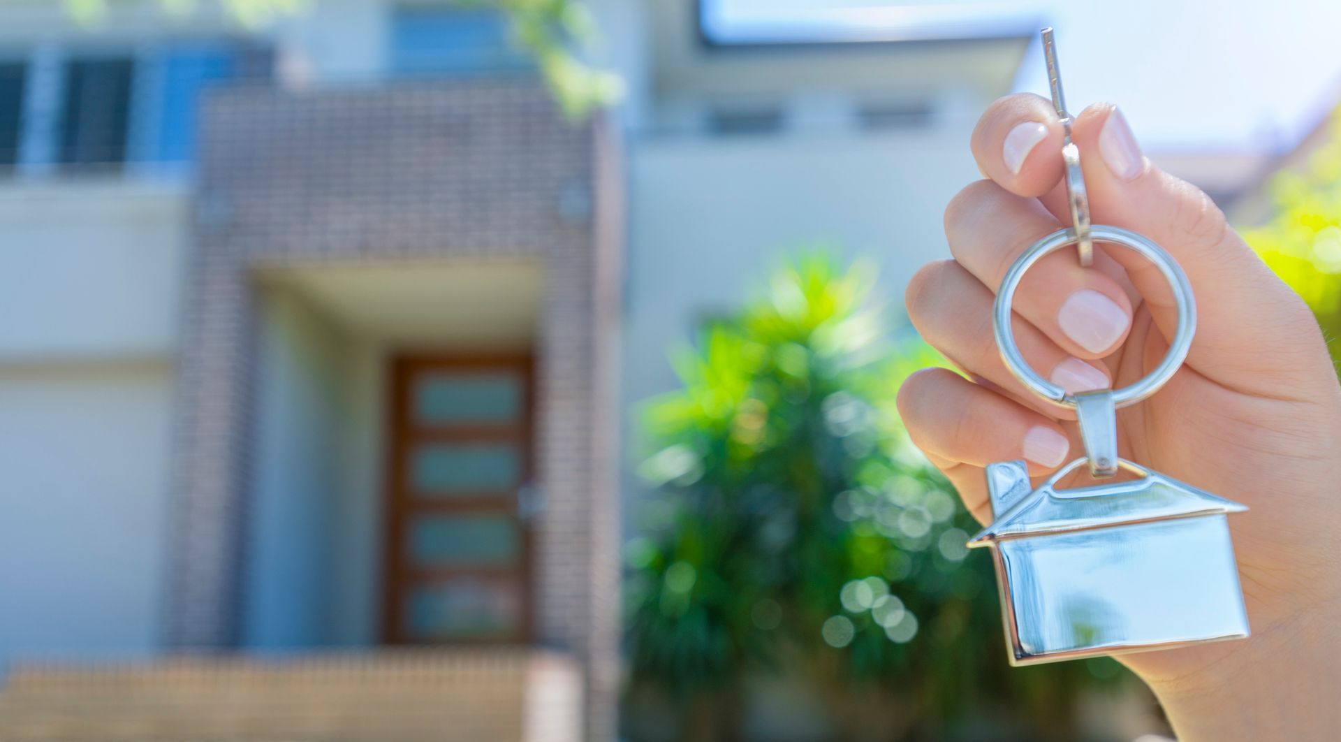 A Person Is Holding A House Key In Front Of A House – Wingfield, SA - On The Spot Locksmiths