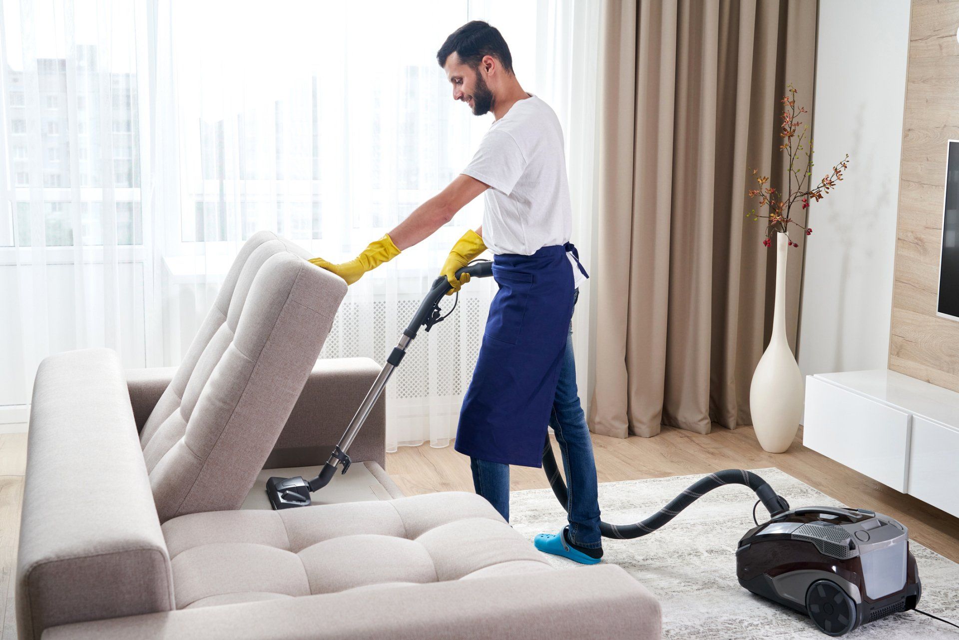 Man Cleaning Sofa With Vacuum Cleaner — Bryan, OH — Sammons Carpet Care Man Cleaning Sofa With Vacuum Cleaner — Bryan, OH — Sammons Carpet Care