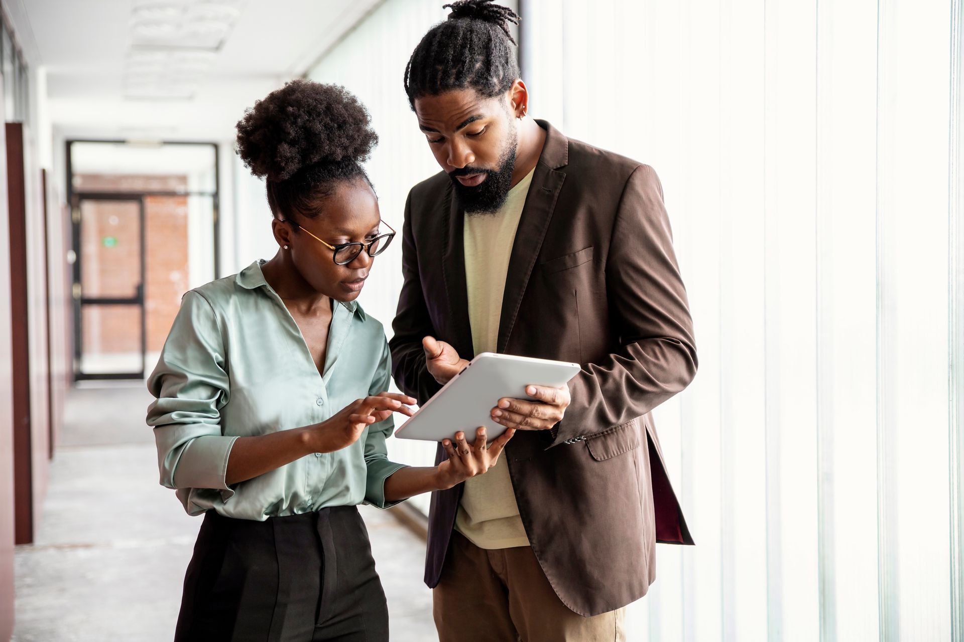A man and a woman are looking at a tablet in a hallway.