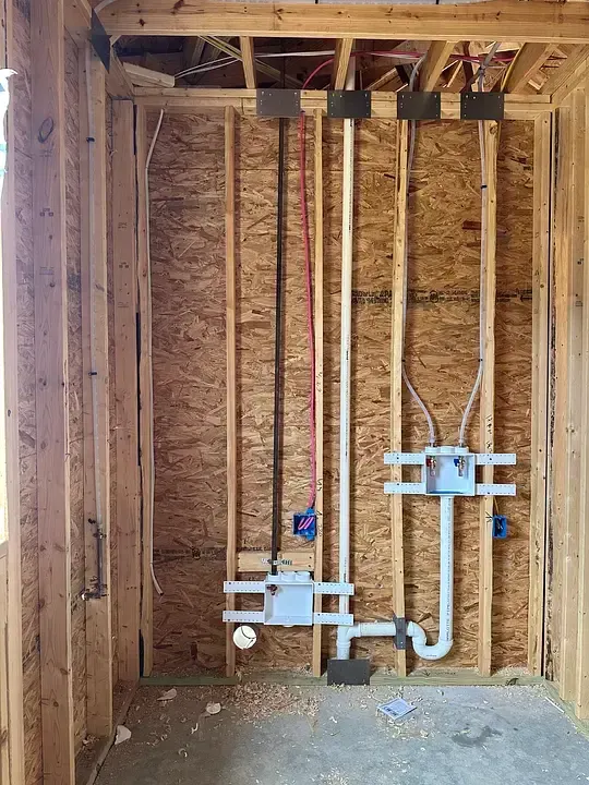Unfinished bathroom wall framing with exposed plumbing pipes and valves