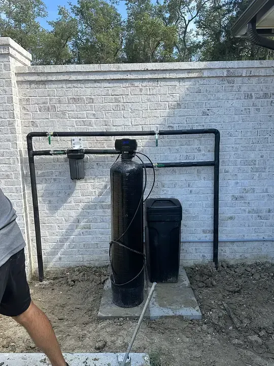 Black water softener tank and resin canister beside a brick wall, with part of a person at left