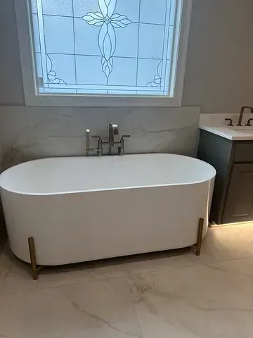 Modern freestanding white bathtub beneath frosted window in a marble-tiled bathroom
