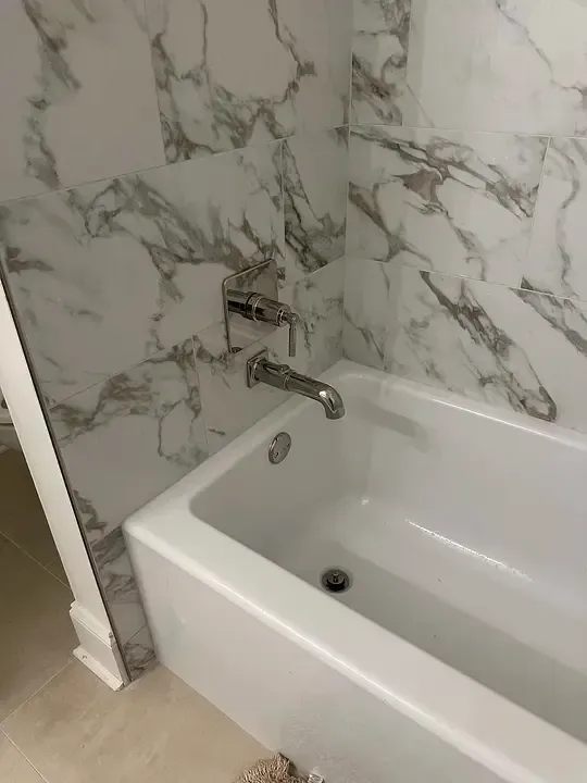 Bathroom with white marble-look walls and a white bathtub with a chrome faucet.