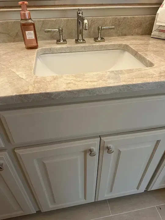 Bathroom sink vanity with white cabinets, beige countertop, and chrome faucet.