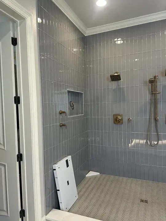 Tiled bathroom shower with glass door, wall niche, handheld showerhead, and leaning white panel on floor