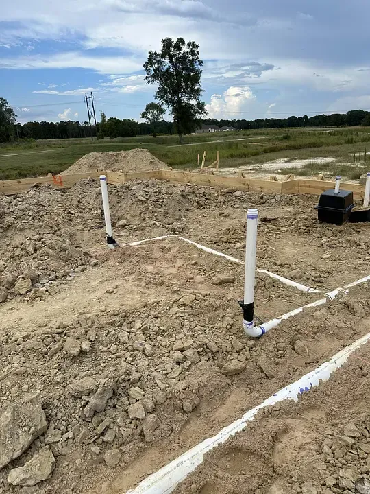Utility pipes in a dirt excavation site with grassy field and tree in the background.