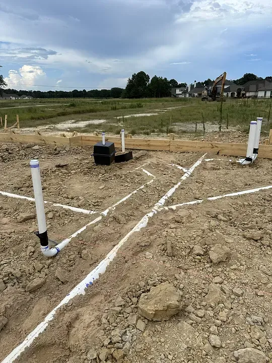 Undeveloped construction site with white PVC pipes and a black utility box in a dirt field.