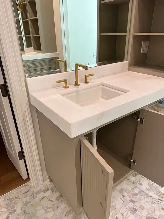 Bathroom vanity with white countertop, gold faucet, open cabinet, and large mirror.