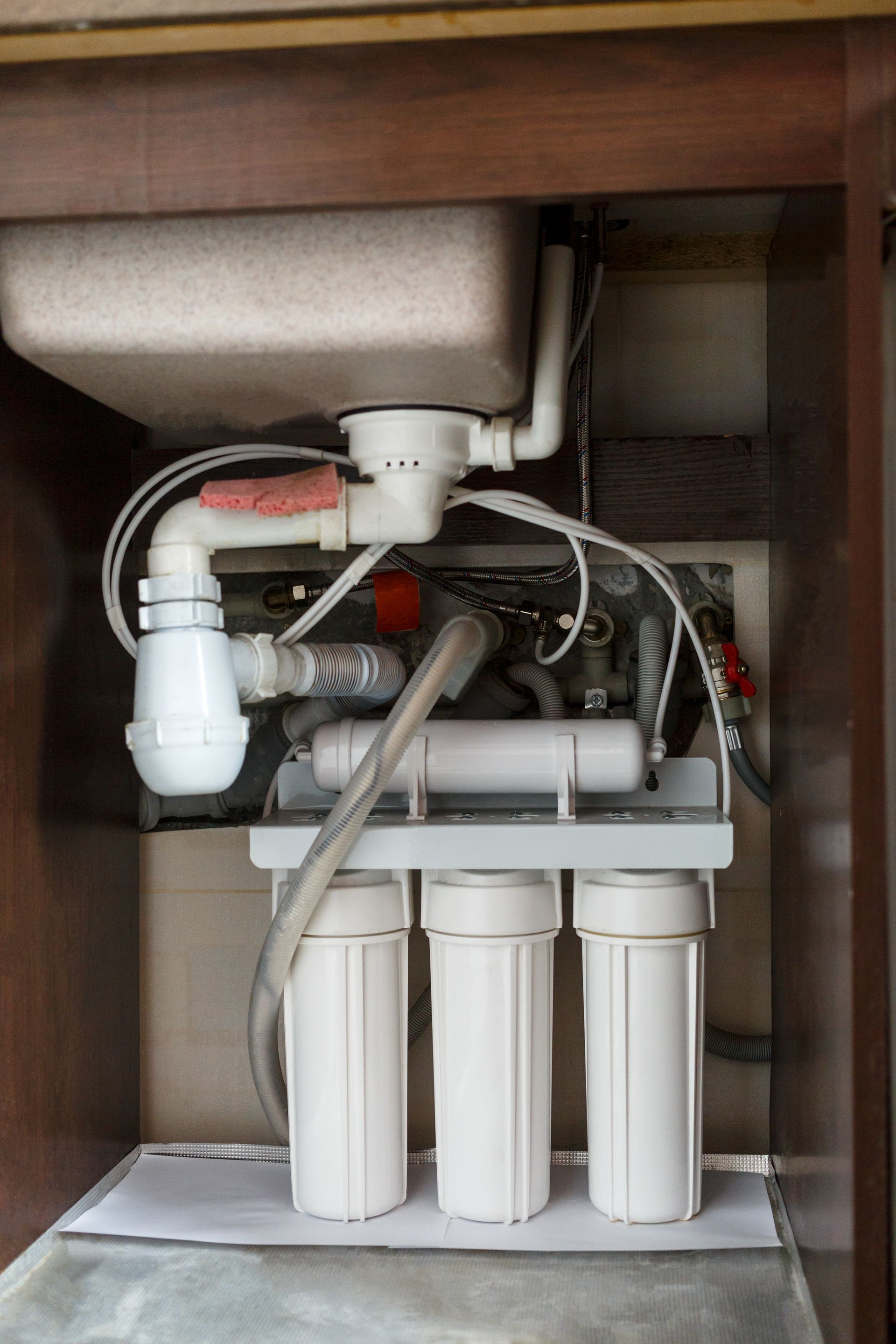 Open cabinet with under-sink water filter system, tubes, and three white filter cartridges